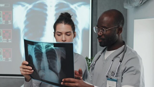 African American and Caucasian interns or medical students holding X-ray shot making diagnosis
