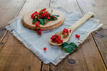 Red currants in a glass. On a wooden background, a light green napkin with leaves and red berries, on a napkin a glass transparent glass with red currant berries.