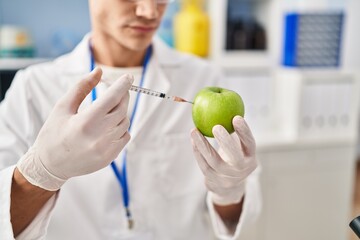 Young hispanic man wearing scientist uniform injecting on apple at laboratory
