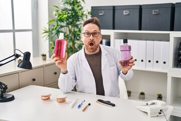 Middle age caucasian dentist man holding mouthwash for fresh breath afraid and shocked with surprise and amazed expression, fear and excited face.