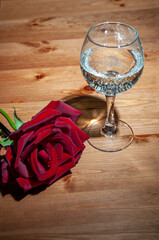 Wine glass with champagne and rose. Stand on a wooden table with texture.