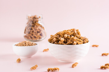 Raw pasta from buckwheat flour in a bowl and groats in a bowl on a pink background