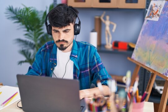 Young hispanic man artist using laptop and headphones at art studio