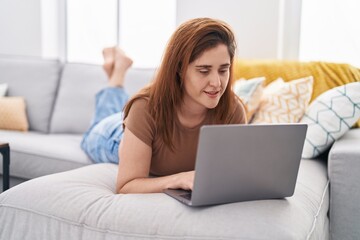 Obraz na płótnie Canvas Young woman using laptop lying on sofa at home