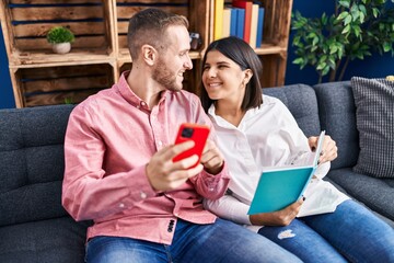 Man and woman couple using smartphone reading book at home