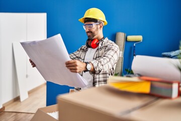Young hispanic man worker smiling confident looking blueprints at new home