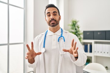 Young hispanic man wearing doctor uniform speaking at clinic