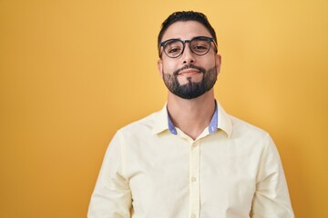 Hispanic young man wearing business clothes and glasses with hands together and crossed fingers smiling relaxed and cheerful. success and optimistic