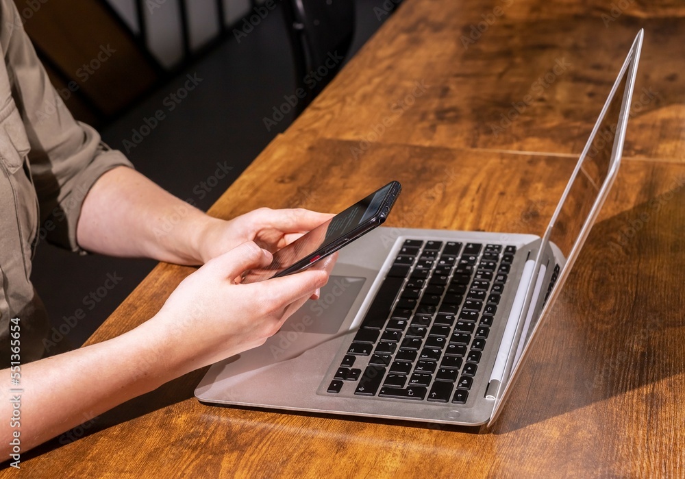 Poster hand holding mobile phone, sitting at wood desk with laptop computer. using information technologies