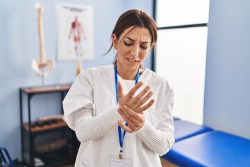 Young brunette woman working at pain recovery clinic suffering pain on hands and fingers, arthritis...
