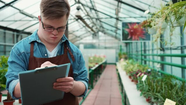 Focused male florist with down syndrome walking and writing in the greenhouse