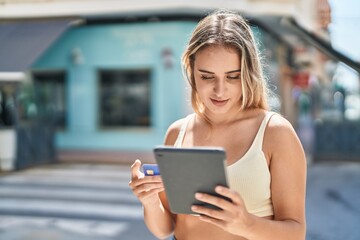 Young blonde woman using touchpad and credit card at street