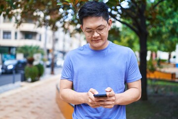 Young chinese man smiling confident using smartphone at park