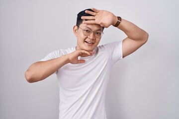 Fototapeta na wymiar Young asian man standing over white background smiling cheerful playing peek a boo with hands showing face. surprised and exited
