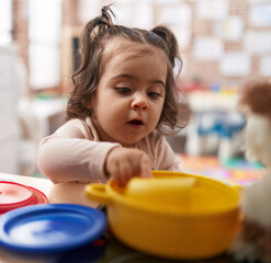 Adorable hispanic girl playing with play kitchen standing at kindergarten