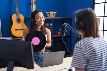 Two women musicians listening to music holding vinyl disc at music studio