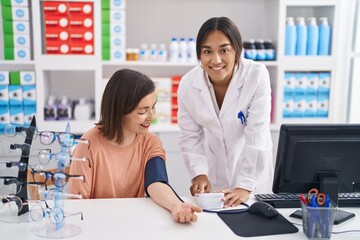 Obraz na płótnie Canvas Two women pharmacist and customer measuring blood pressure at pharmacy