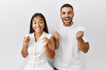 Young interracial couple standing together in love over isolated background celebrating surprised...
