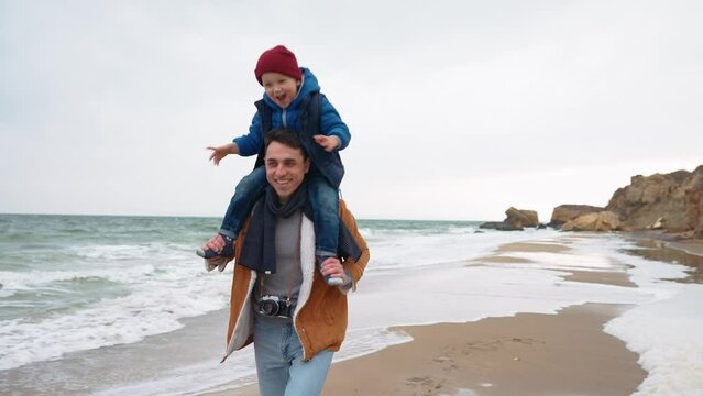 Happy father running with his son on his neck on the beach near the sea