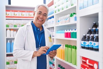 Middle age grey-haired man pharmacist using touchpad working at pharmacy