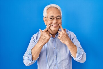 Hispanic senior man wearing glasses smiling with open mouth, fingers pointing and forcing cheerful smile