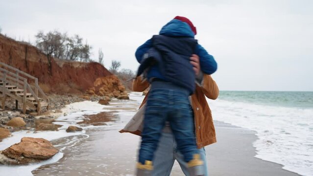 Funny father twirls his son in his arms on the beach near the sea