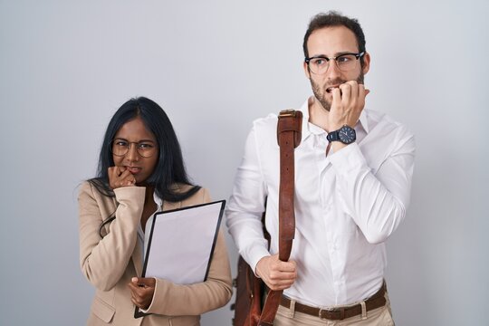 Interracial business couple wearing glasses looking stressed and nervous with hands on mouth biting nails. anxiety problem.