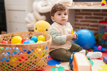 Fototapeta na wymiar Adorable hispanic toddler playing with balls sitting on floor at kindergarten