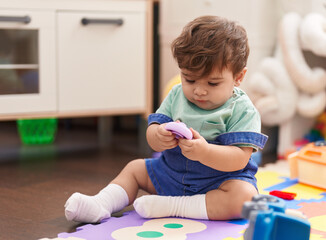 Adorable hispanic toddler sitting on floor with serious expression playing at kindergarten