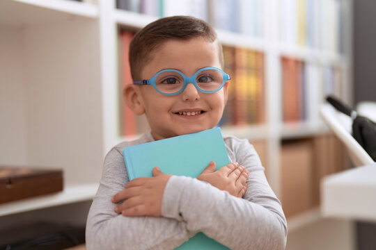 Adorable hispanic toddler student smiling confident holding book at library school