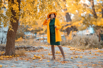 Beautiful woman walks outdoors in autumn. She is wearing a yellow coat, yellow hat and green dress. Young woman enjoying the autumn weather. Autumn content