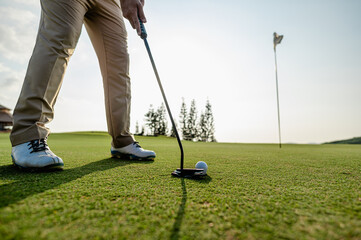 Golfer man aiming at golf ball in a ready position to hitting golf hole on the green grass during the day.
