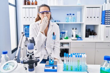 Young hispanic woman working at scientist laboratory bored yawning tired covering mouth with hand. restless and sleepiness.