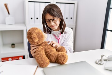 Young hispanic girl checking teddy bear health at doctor clinic