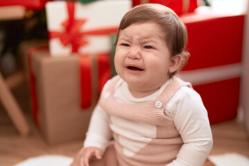 Fototapeta premium Adorable toddler sitting on floor by christmas gift crying at home