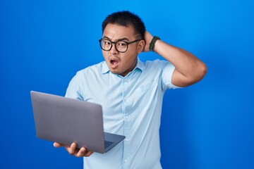 Chinese young man using computer laptop crazy and scared with hands on head, afraid and surprised of shock with open mouth