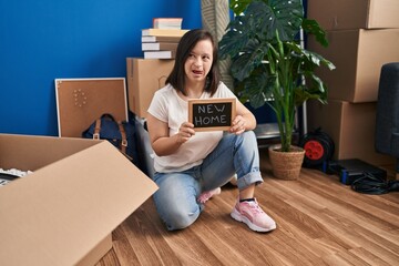 Hispanic girl with down syndrome sitting on the floor at new home sticking tongue out happy with funny expression.