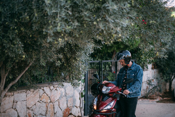 Naklejka premium A young man in a helmet starts a motorcycle near the gate of the house.