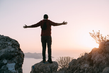 A young man meets the sunset, arms outstretched in a free gesture on a mountain by the sea.