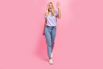 Full length portrait of cheerful lovely person toothy smile arm palm waving walking isolated on pink color background