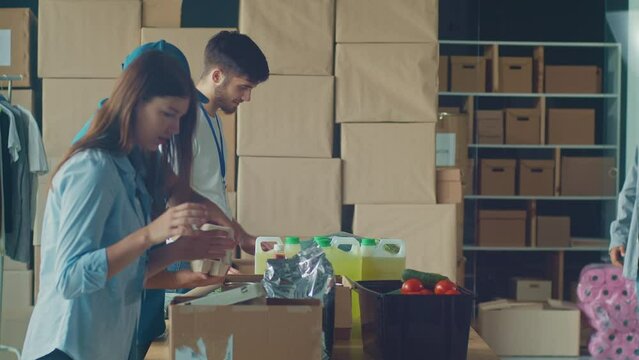 Friendly Volunteer Giving Donation Box With Food to Man and His Son at Distribution or Refugee Assistance Center. The Concept of Social Aid. Internally Displaced Persons