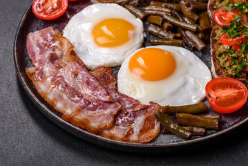 Tasty breakfast consists of eggs, bacon, beans, tomatoes, with spices and herbs