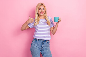 Photo of smiling blonde hair business lady wear trendy t-shirt thumb up like symbol hold cup morning coffee isolated on pink color background