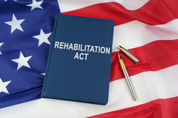 On the US flag lies a pen and a book with the inscription - REHABILITATION ACT