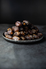 Dates fruit on oriental plate on dark background. Dried organic Superfood