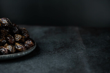 Dates fruit on oriental plate on dark background. Dried organic Superfood