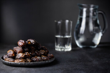 Dates fruit on oriental plate on dark background. Dried organic Superfood. Water for Ramadan fasting. Traditional muslim iftar food