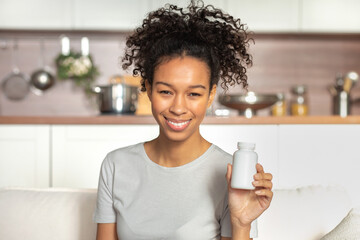 Happy young African American woman holding bottle of dietary supplements or vitamins in her hands....