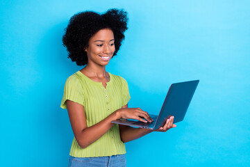 Obraz na płótnie Canvas Photo of positive clever girl with perming coiffure dressed green t-shirt hold laptop doing homework isolated on blue color background
