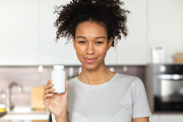 Happy young African American woman holding bottle of dietary supplements or vitamins in her hands....